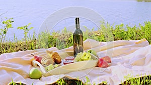 Picnic by the river. On a light-colored bedspread, a wooden tray with fruit, cakes and a bottle of wine.