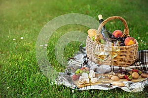 Picnic setting with  two glasses of white wine,  cheese, fruits and basket. Outdoor, green lawn