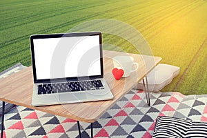 Picnic table with blank screen on laptop and white coffee cup, r