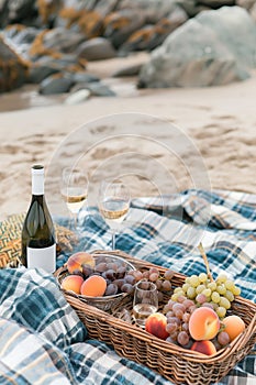 Picnic with wine and fruit in a wicker basket on a sandy beach by the sea.