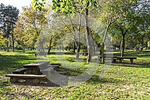 Picnic wooden tables and benches on a green lawn among the trees in Bundek city park, Zagreb, Croatia