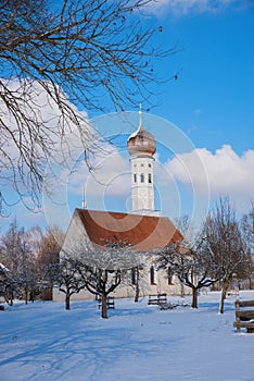 Pictorial bavarian church in winter landscape, bare-leaved apple trees