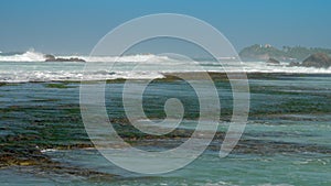 Pictorial ocean waves roll on brown rocks at coastline