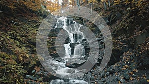 Pictorial waterfall flows over grey large rocks in autumn