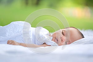Picture of an Asian newborn baby sleeping peacefully on a long coat in an Asian garden