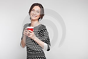 Picture of attractive woman in speckled clothes standing with cup in hands