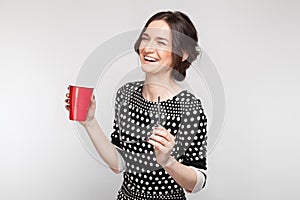 Picture of attractive woman in speckled clothes standing with cup in hands
