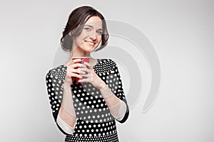 Picture of attractive woman in speckled clothes standing with cup in hands