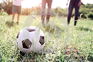 A picture of ball lying in grass. There are members of one family playing with it. They are ready to push ball. They are
