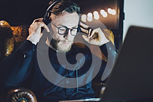 Picture bearded man wearing glasses relaxing modern loft office.Hipster sitting vintage chair,listening music laptop