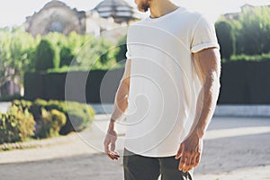 Picture Bearded Muscular Man Wearing White Blank t-shirt. Green City Garden Background at sunset. Horizontal Mockup