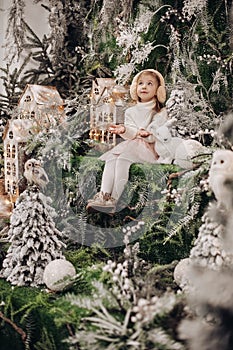 picture of beauatiful little girl rejoices of a christmas decoration with trees and a little white rabbit