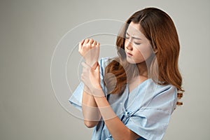 A picture of a beautiful Asian woman in a patient`s dress with wrist pain due to symptoms of Office syndrome on a gray background