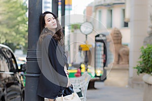 A picture of a beautiful long haired Asian lady in a black robe standing and looking out in the city outdoors