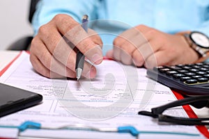 Picture of clipboard, form, glasses, calculator, pen and phone. Man is holding pen in hand