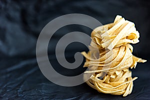 Picture of column from traditional Italian raw uncooked pasta Tagliatelle on black crumpled paper backgrpond, selective focus.