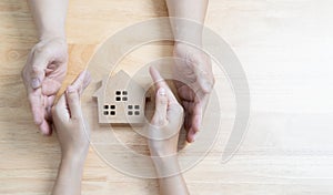 Picture of couple hands over and presenting to safe and take care of a small model of house