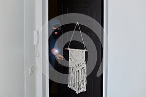 Picture of dangerous burglar breaking into house, wants to steal belongings and money, opening door and shining a flashlight to