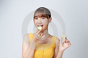 A picture of a face of a beautiful woman posing with a cucumber over white background