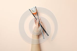 Female hand hold chopsticks with roll on beige background