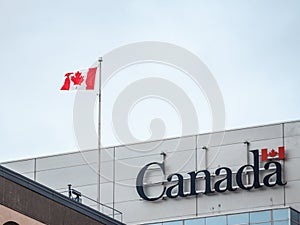 Canada Wordmark, the official logo of the Canadian government, on an administrative building next to a Canadian flag waiving