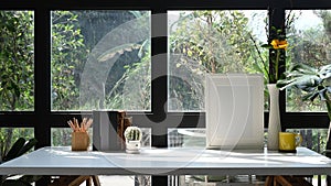 Picture frame, coffee cup, books and plower pot on white table near glass window.