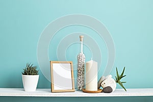 Picture frame mockup. White shelf against pastel turquoise wall with Candle and rocks in bottle.