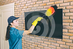 A picture of girl cleaning TV from dust. She ues dust brush. It is colorful. Girl works with pleasure.