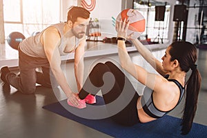 A picture of girl doing some abs exercise with the ball while her sport partner is holding her legs down on the floor