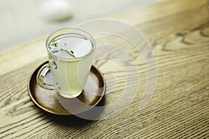 Picture or glass cup with green or white tea in it. Stand on plate. No people aroun. Daylight. Close up.