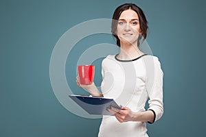 Picture of good looking woman in light clothes standing with coffe and recordings in hands