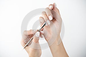 Picture of hands using cuticle pusher while doing manicure on isolated while background