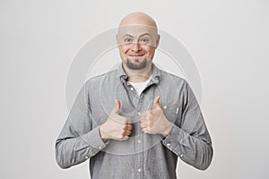 Picture of happy handsome guy in casual gray shirt holding his thumbs up in approving gesture over white background