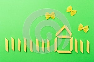 Picture with house made from penne type of italian pasta and farfalle butterflies on green background. Home made italian pasta
