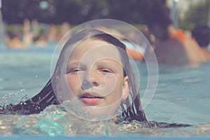 A picture of a little girl at a swimming pool in summer. A small girl swimming to the edge of a swimming pool at a swimming pool.