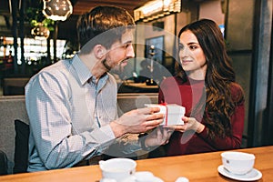 Picture of man giving a present to a woman. They are looking to each other and smiling a bit. They are sittin in