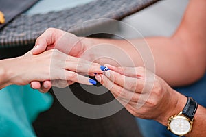 Picture of man putting engagement silver ring on woman hand, outdoor.