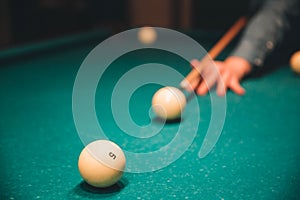 Picture of man`s hand holding billiard cue and aiming to breal ball. he plays inside on bed of table.