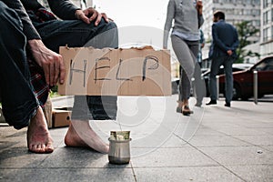A picture of man`s legs without shoes standing on the concrete ground. There is a metal cup with money on it. Guy is
