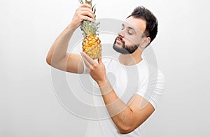 Picture of man standing and holding pineapple. He looks at it with seriousness. Isolated on white background.