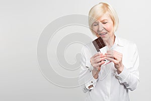 A picture of mautre lady eading a bar of milk chocolate. She likes to eat sweets. She cares about her health a lot but photo