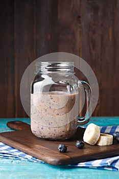 Picture of mug with milkshake with banana and berries on cutting board at wooden background