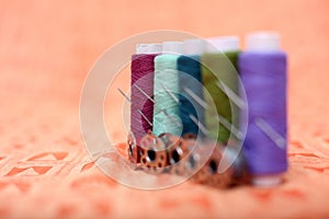 Picture of multicolored sewing thread, needle and bobbin on the orange cloth