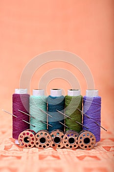 Picture of multicolored sewing thread with needle and bobbin on the orange cloth