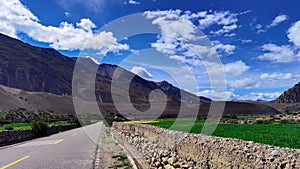 A picture of natural scenery composed of mountains, roads, and fields under blue sky and white clouds.