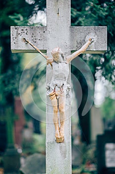Picture of old wooden or stone cross with figure of crucified Jesus Christ. Memory on grave or cementary. Green trees on