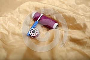 Picture of one sewing thread, needle ripper and bobbin on the golden cloth