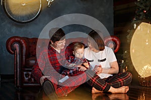Picture of parents sitting together with their child on the floor. They are looking at him. Kid is playing on th phone