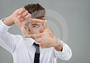 Picture perfect. A young man wearing a shirt and tie framing his eye between his fingers.
