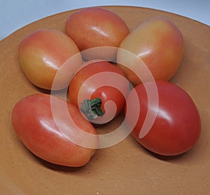 A picture of a pile of tomatoes placed on a clay plate.